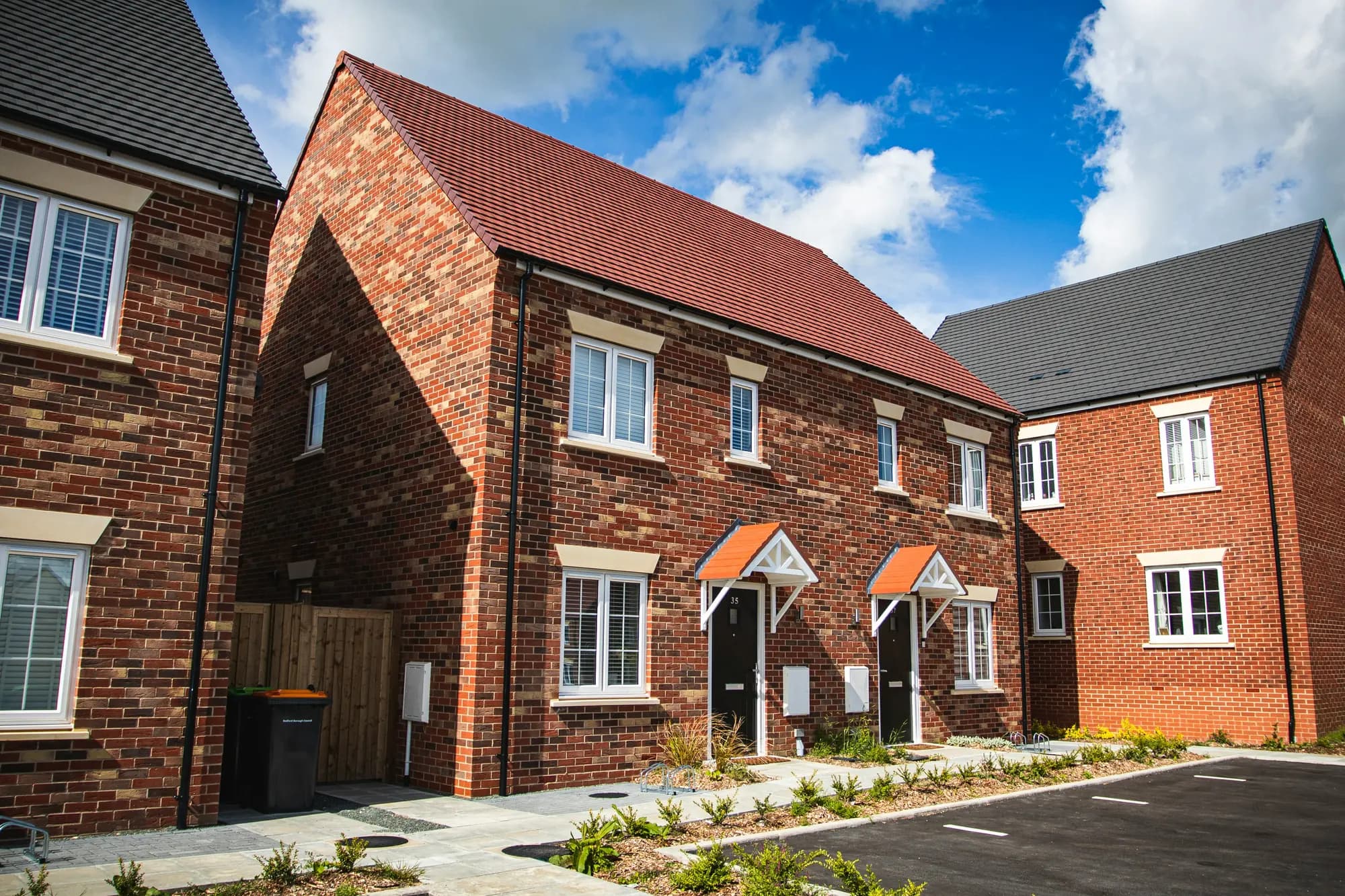 Red-brick new-build homes on a modern residential street under a bright blue sky